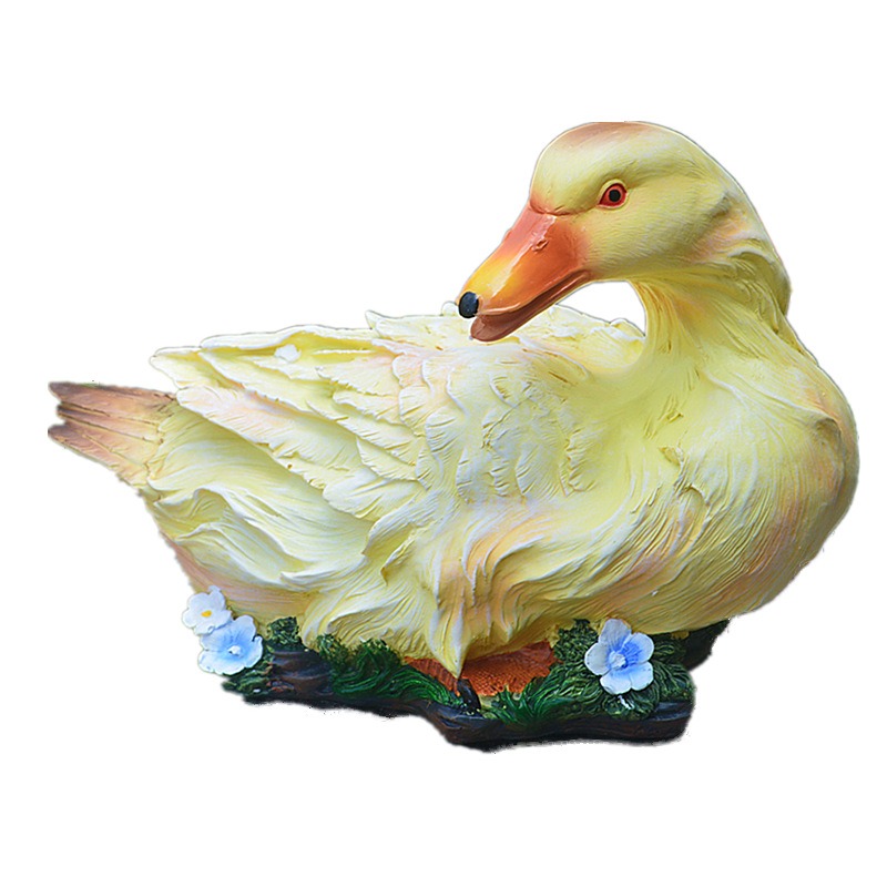 Yellow resin duck with orange beak set among blue flowers on grass