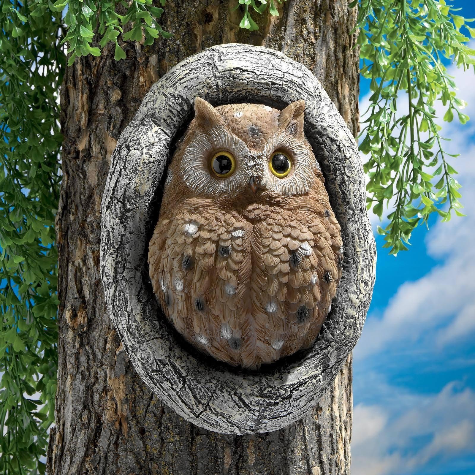 Owl hanging board mounted on a tree trunk with green leaves behind