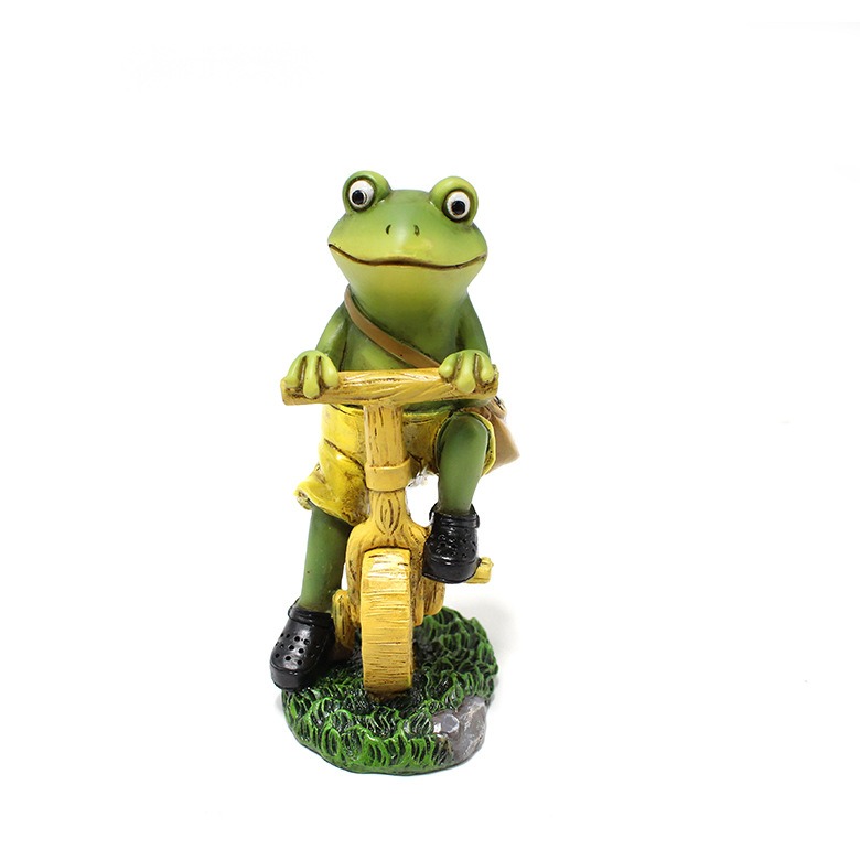 Front view of a frog figurine gripping the handlebar on a grass base
