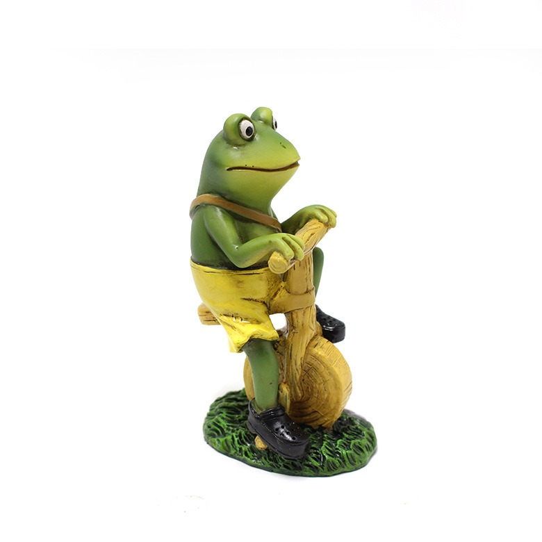 Side profile of a frog figurine on a bicycle beside a garden bed