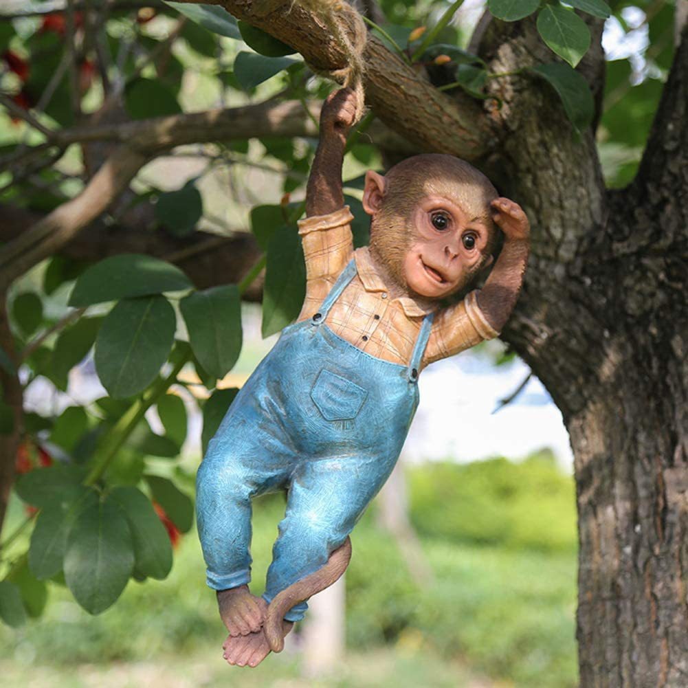 Blue-overall resin monkey hanging from a tree branch outdoors