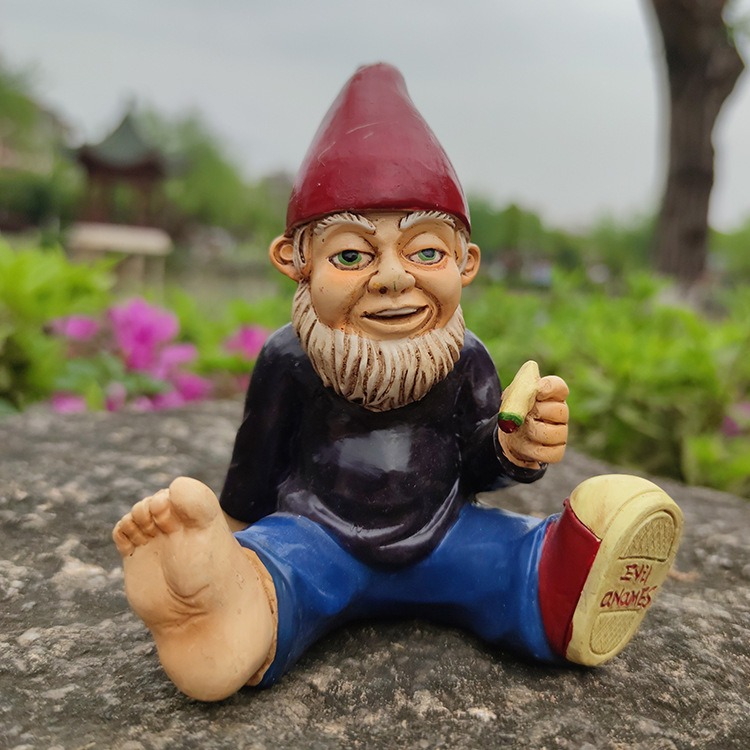 Gnome figurine on grey stone with pink flowers and garden behind