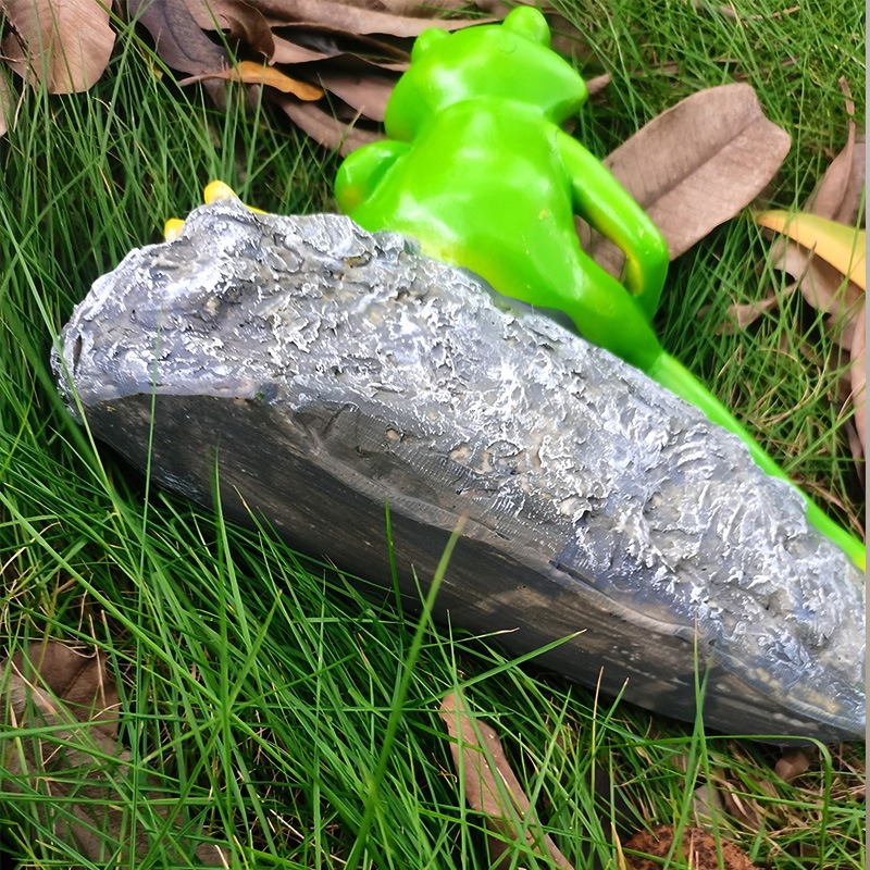Side view of a textured grey stone base with frog legs among the grass