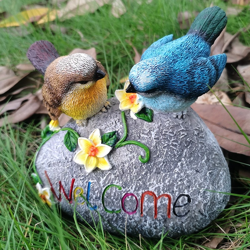 Painted resin birds on a stone in a lawn with dry leaves