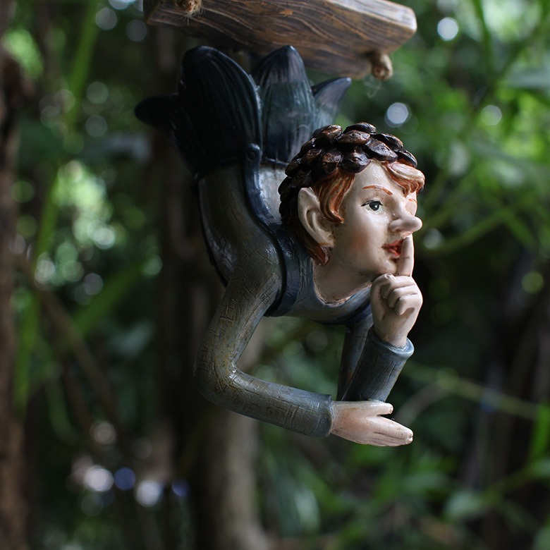 Close profile of painted elf on swing against garden greenery
