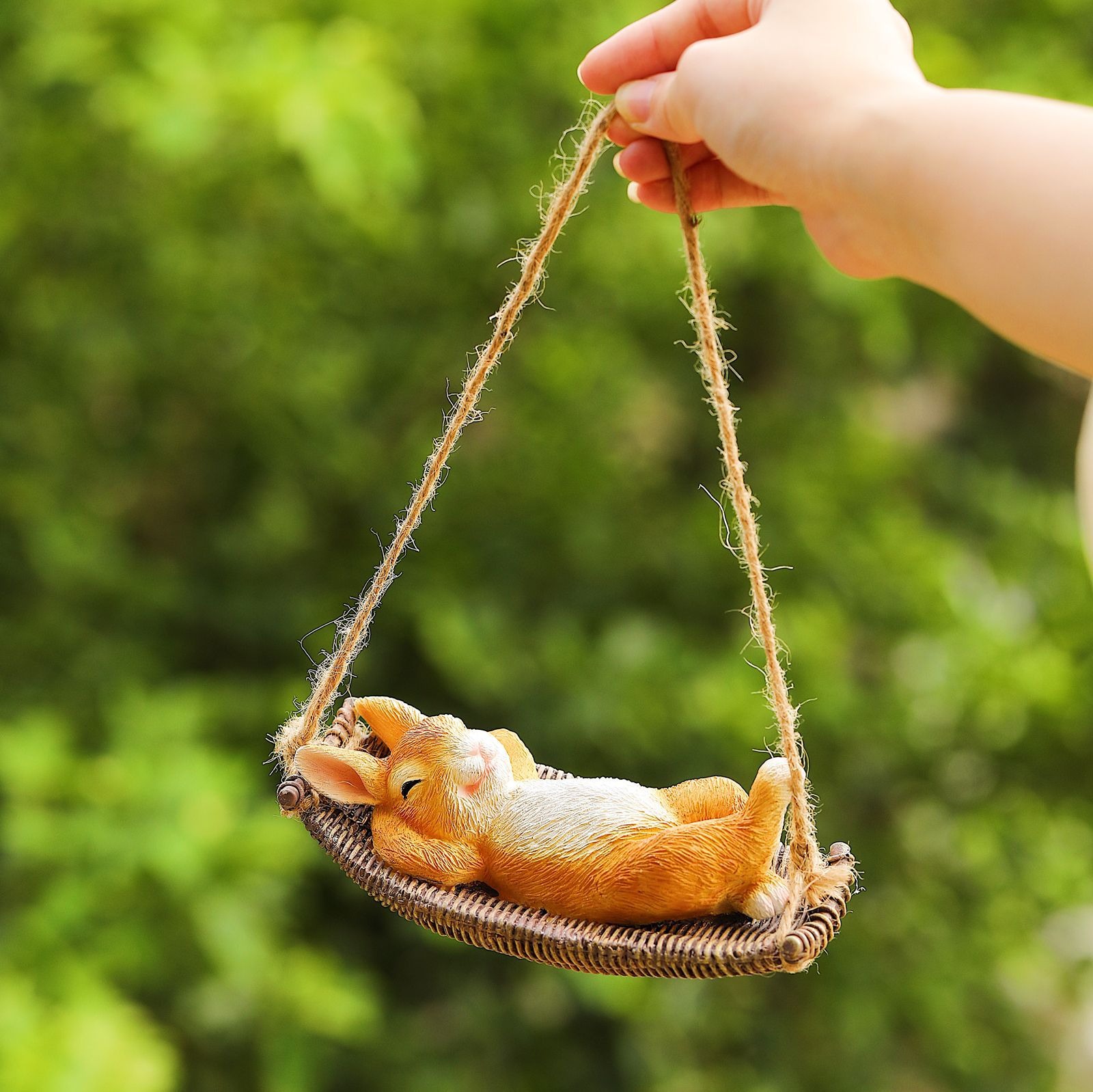 Hand holding the rabbit swing by rope against green foliage