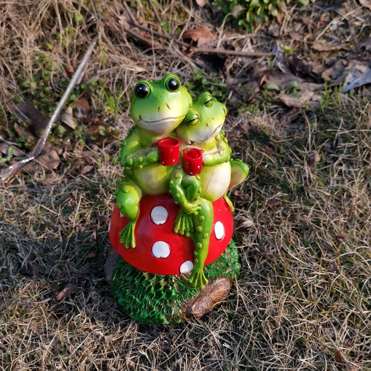 Frog mushroom sculpture set into a garden bed beside a stone accent