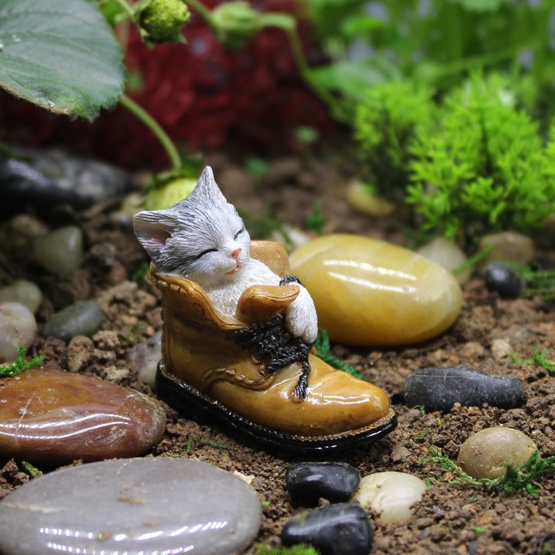 Cat-in-boot figurine set among pebbles and moss in a micro landscape