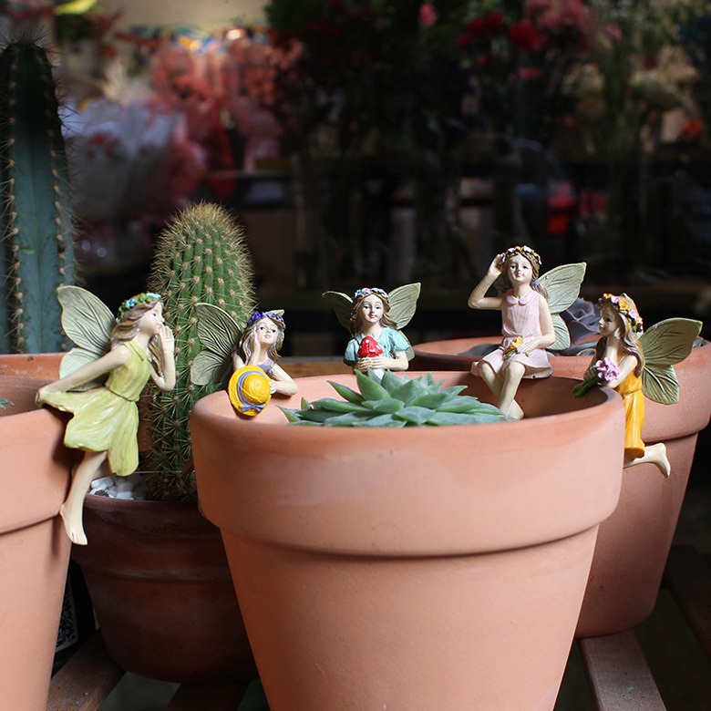 Five fairy figures sitting on terracotta pots among succulents and a cactus