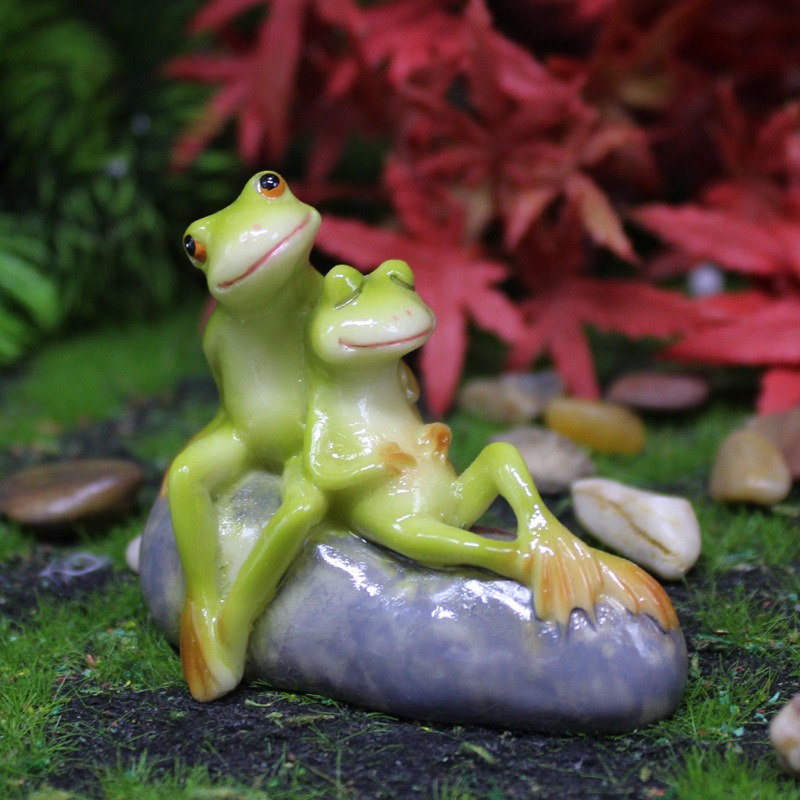 Frog couple figurine placed on mossy ground among small stones in a garden