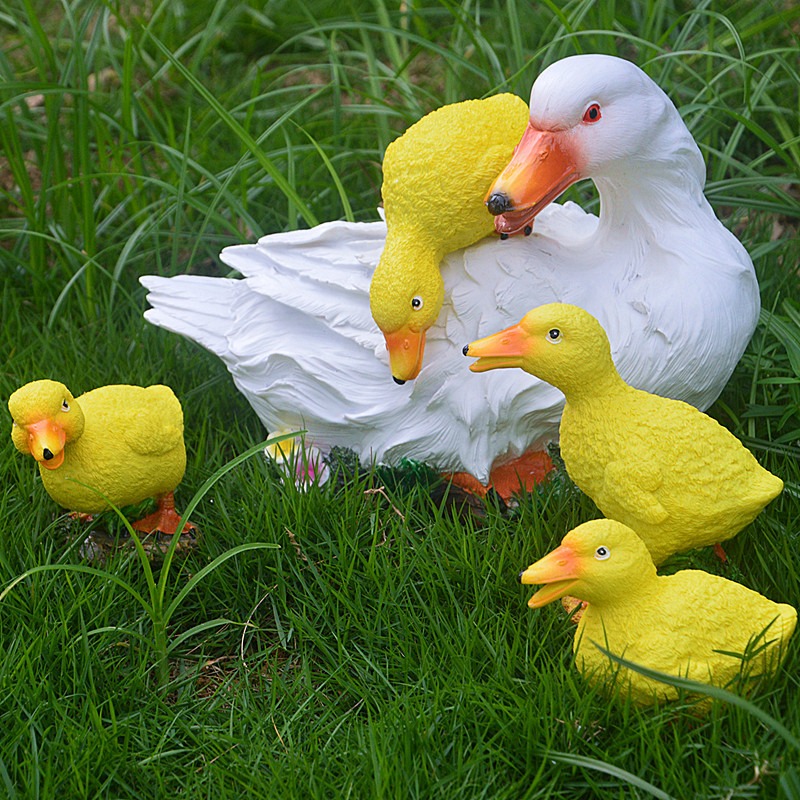 Yellow and white resin ducks arranged on grass in a garden