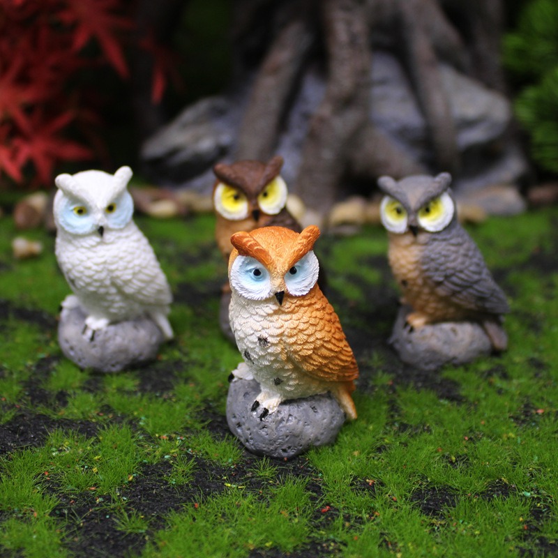 Owl figurines among green moss and tree roots in a miniature garden