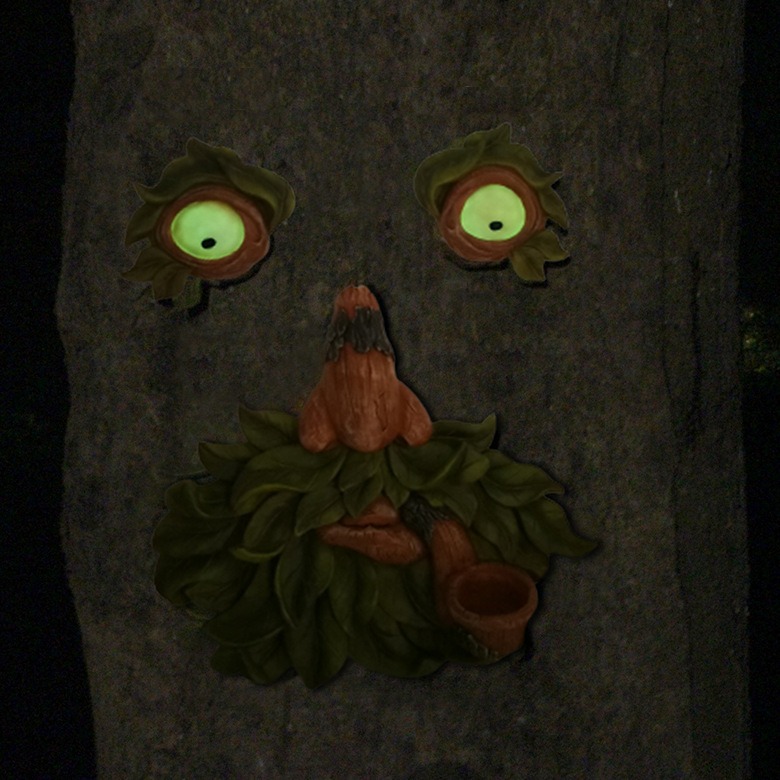Resin tree face with bright green glowing eyes in a dark garden