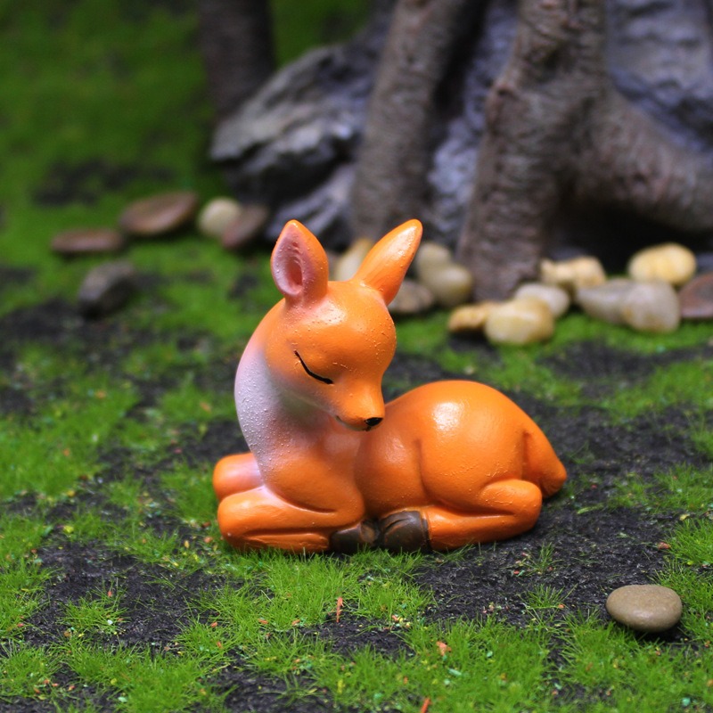 Doe figurine resting on moss with pebbles and tree roots behind