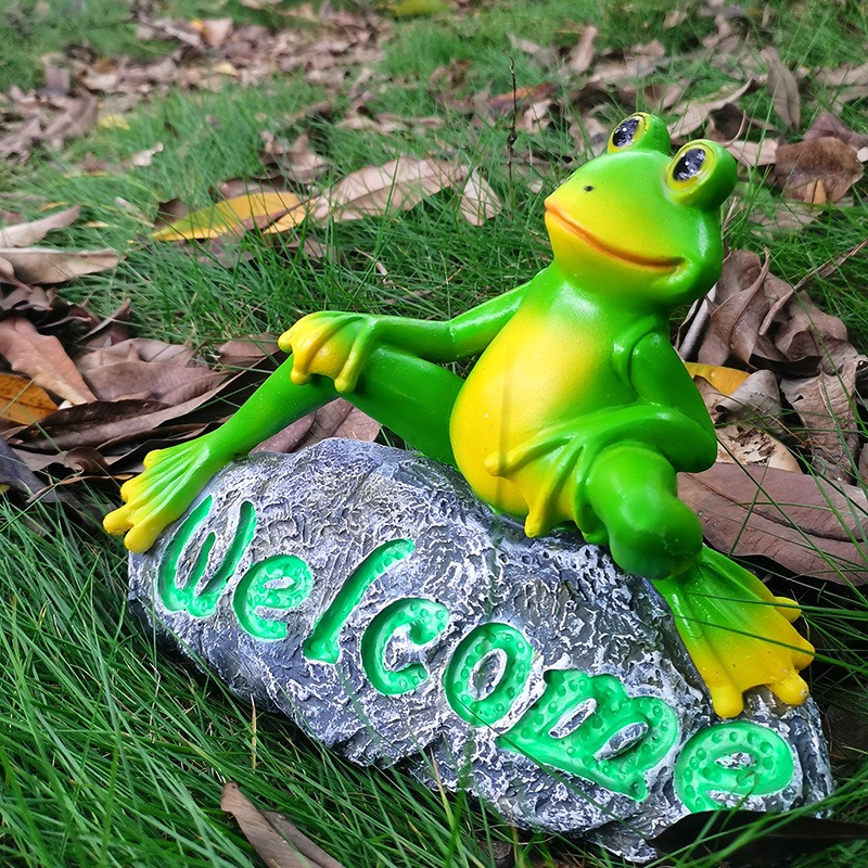 Frog welcome ornament sitting in grass with autumn leaves around it