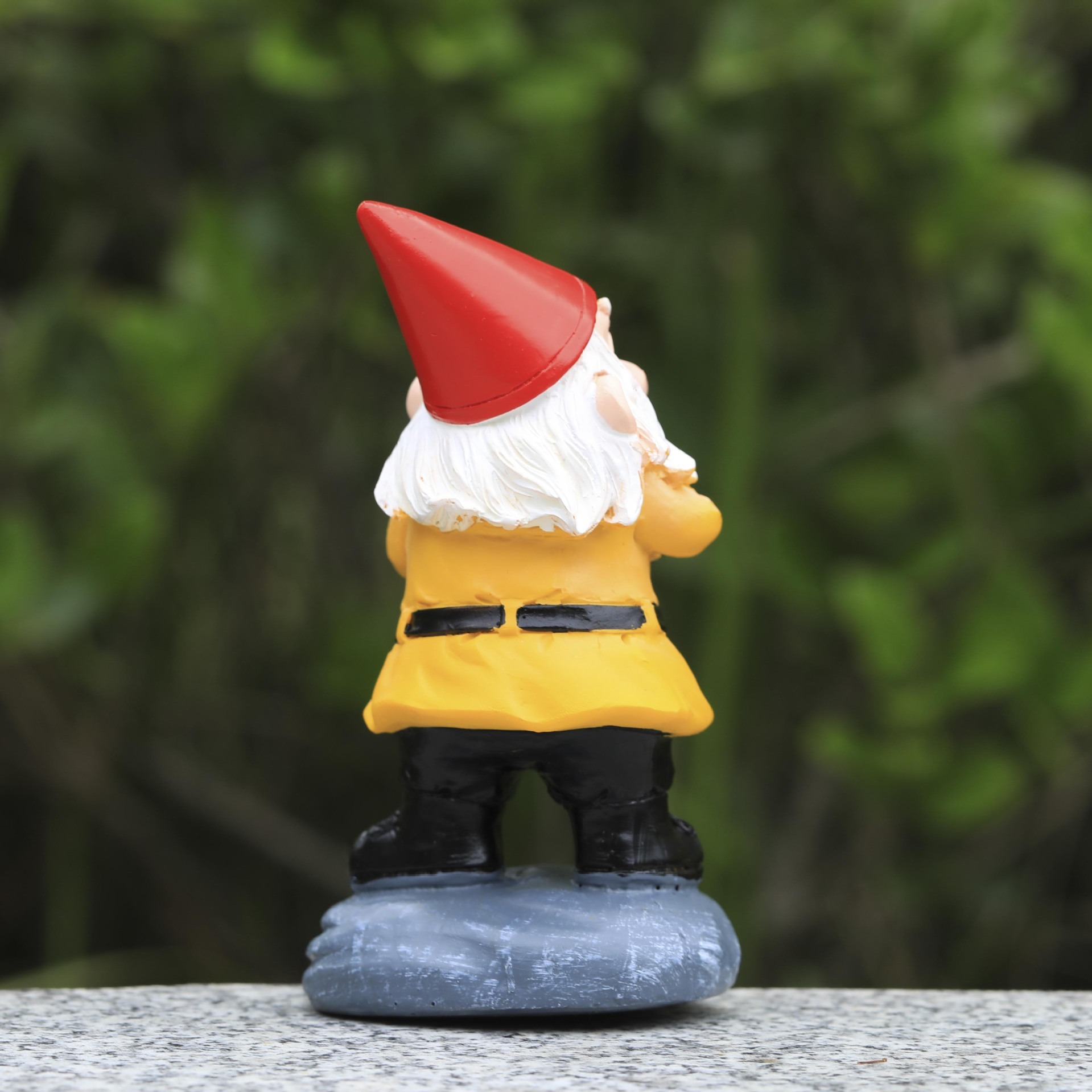 Garden gnome set on a stone ledge among green foliage outdoors