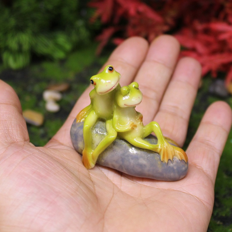 Miniature couple frog figurine held in an open palm at true scale