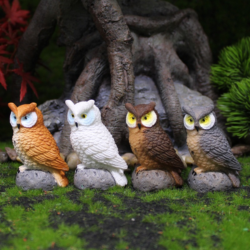 Four owls on stone bases in a row on moss with tree roots behind