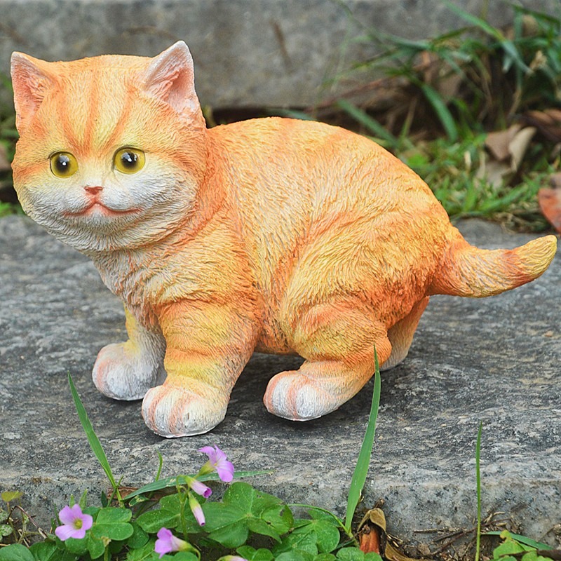 Orange tabby cat ornament on a stone slab beside purple flowers