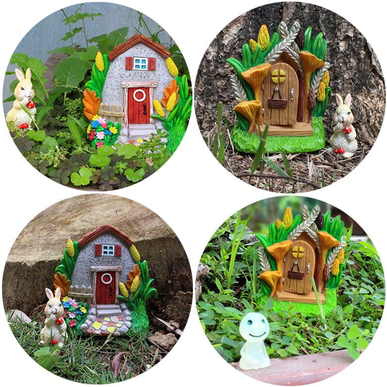 Cottage and fairy door set in grass beside flowers and a tree trunk