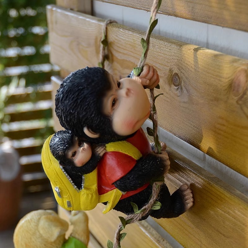 Black monkey figurine in yellow vest climbing a jute rope against a wooden fence
