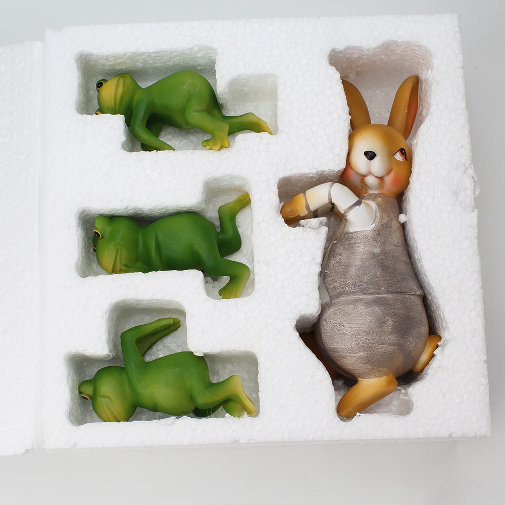 Green frog figurines and a grey rabbit nestled in white foam trays