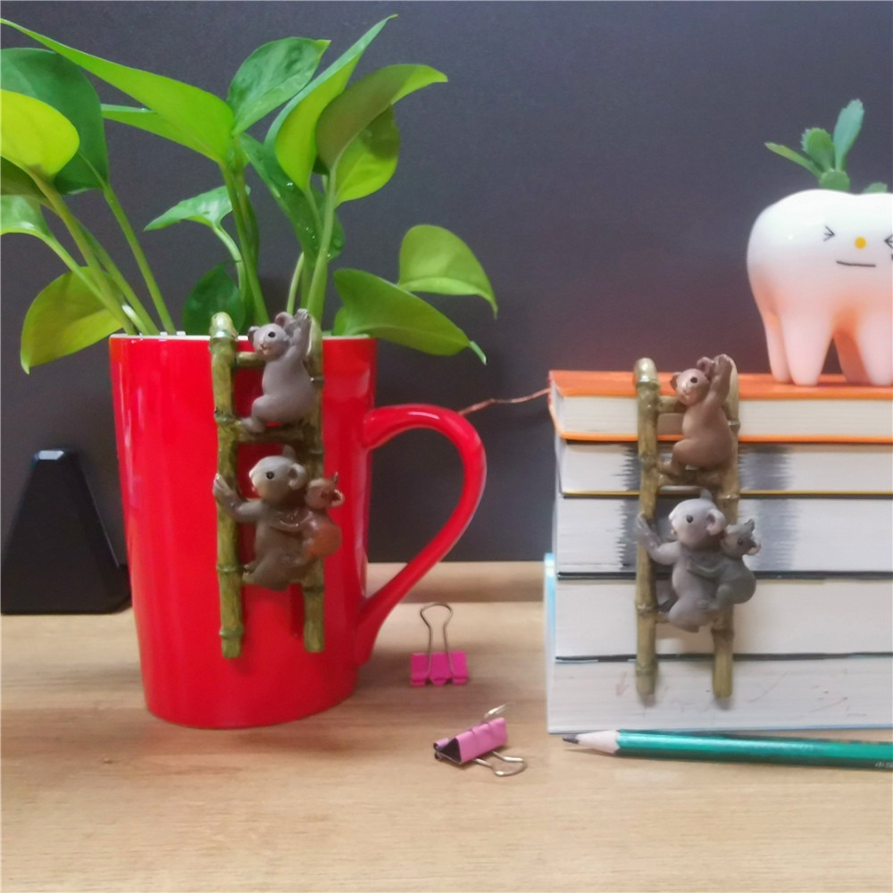 Koala ladder hanging from the rim of a red mug beside a plant