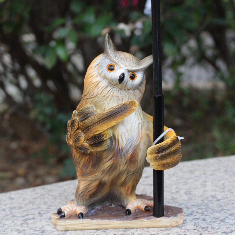 Close-up side view of owl figurine holding black stake on a garden stone ledge