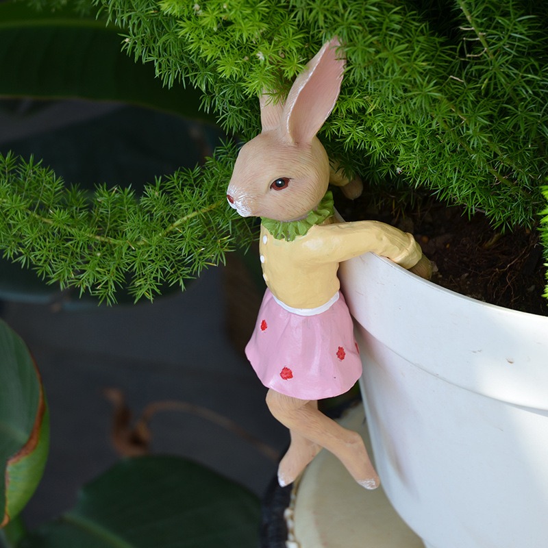 Pink-skirted bunny hanging over a white flower pot with fern foliage