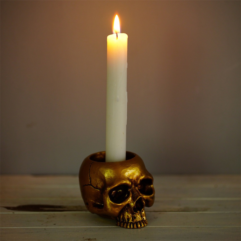Golden skull holder with a white pillar candle burning in its crown