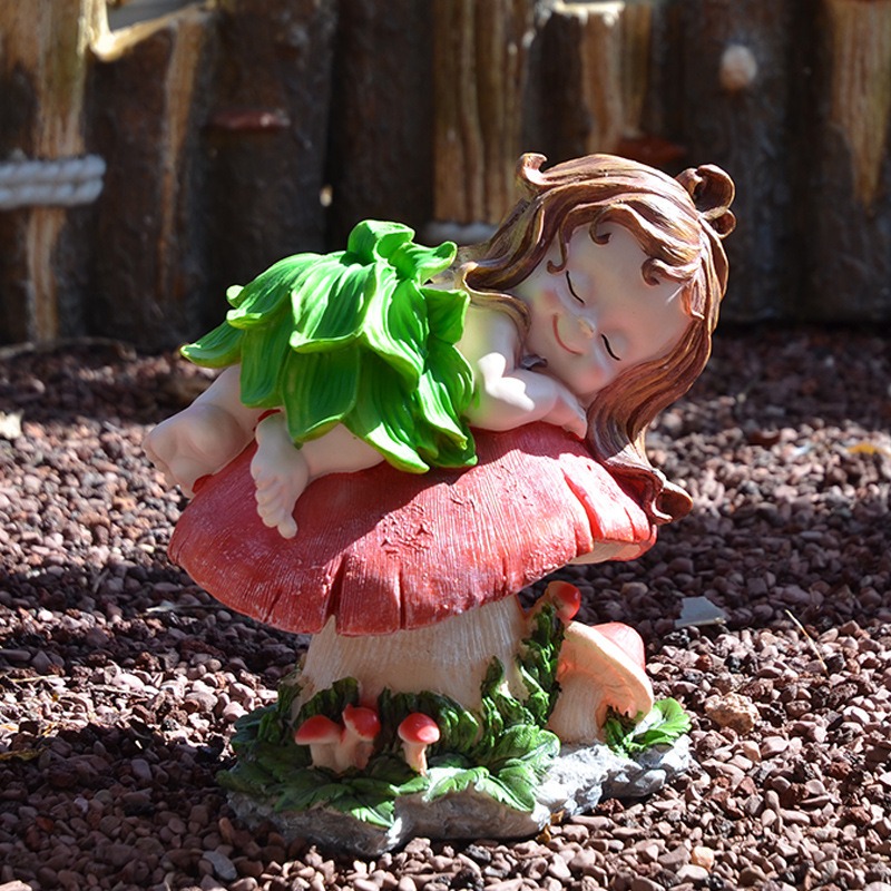 Garden elf ornament placed outdoors on pebbles beside a red mushroom