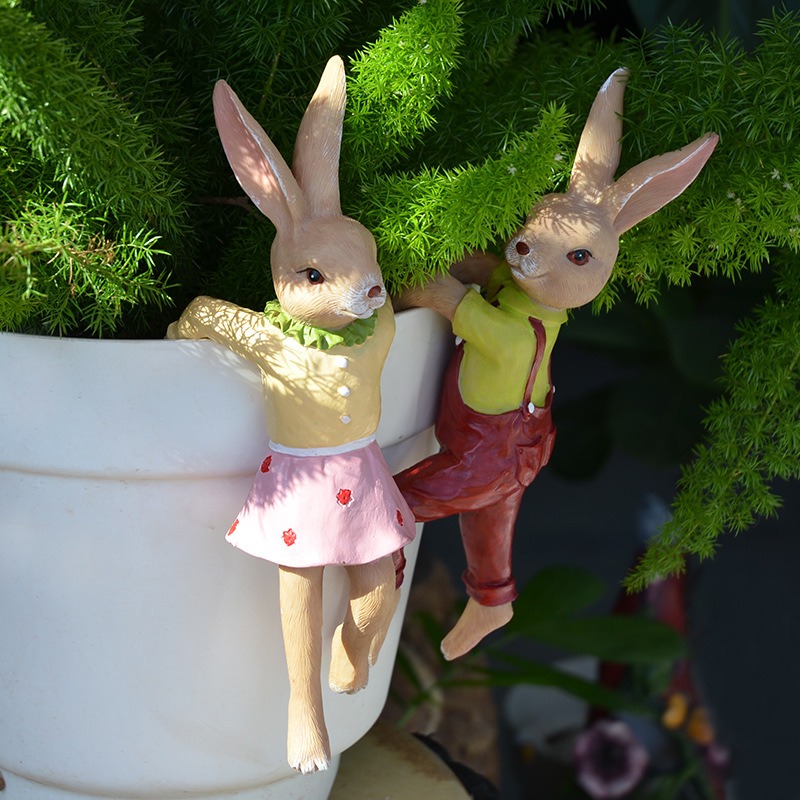 Two bunny figurines perched on a white planter among green fern leaves