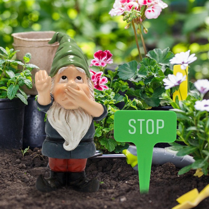 Gnome and STOP stake placed in soil among geraniums and garden tools