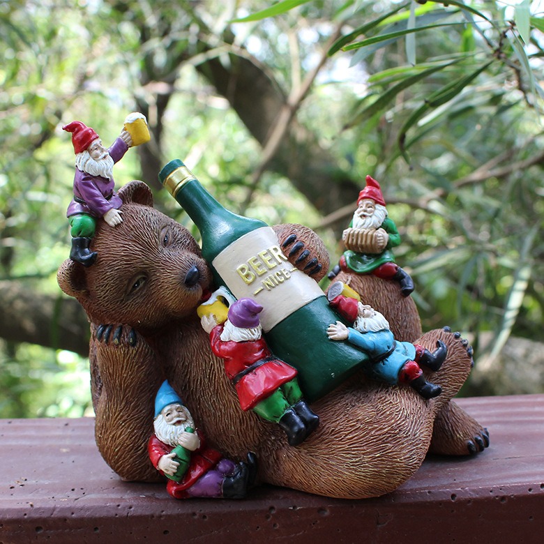 Bear gnome garden sculpture placed on a wooden ledge outdoors among foliage