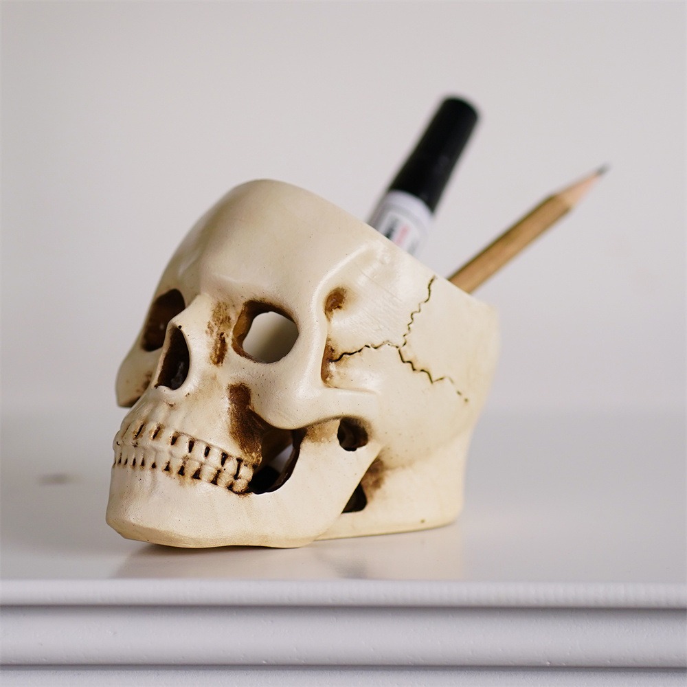 Resin skull on a desk holding a black marker and a wooden pencil