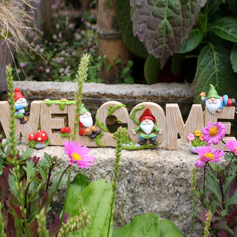 Gnome welcome sign on a stone ledge among flowers and greenery
