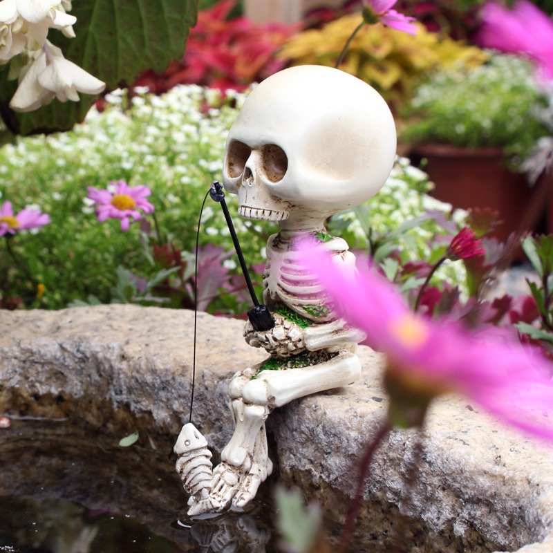Skeleton figurine perched on a stone pond edge among garden flowers