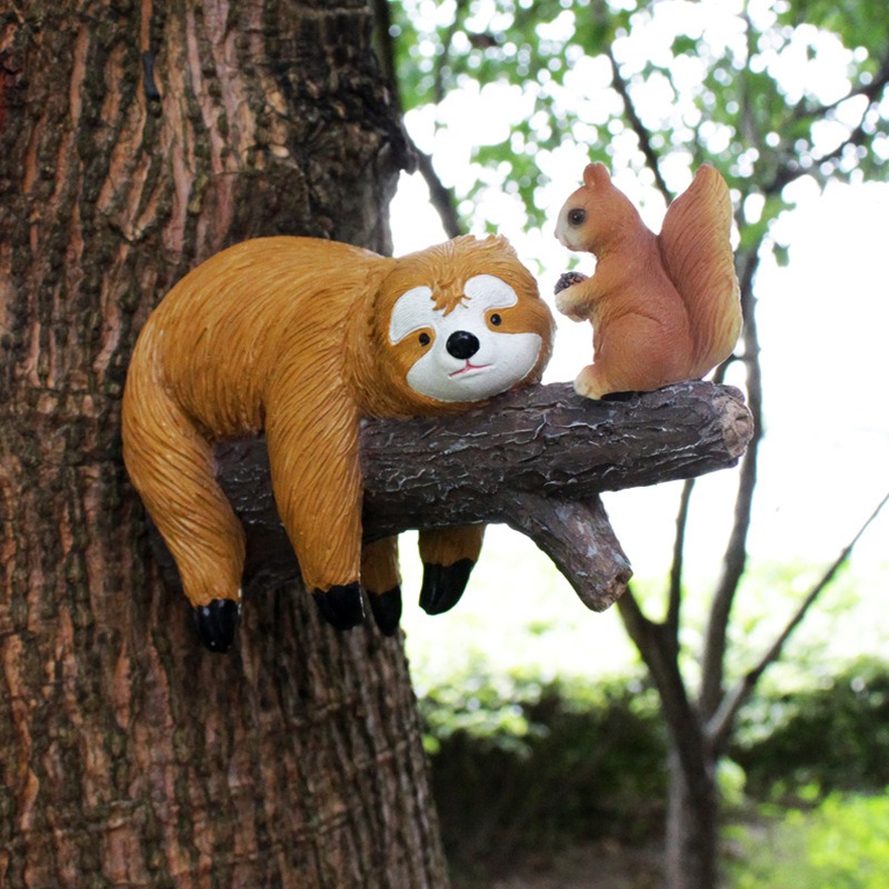 Close-up of sloth and squirrel decor against green leaves on a tree