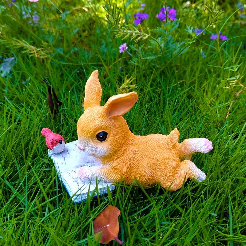 Bunny reading ornament set in green grass beside purple wildflowers