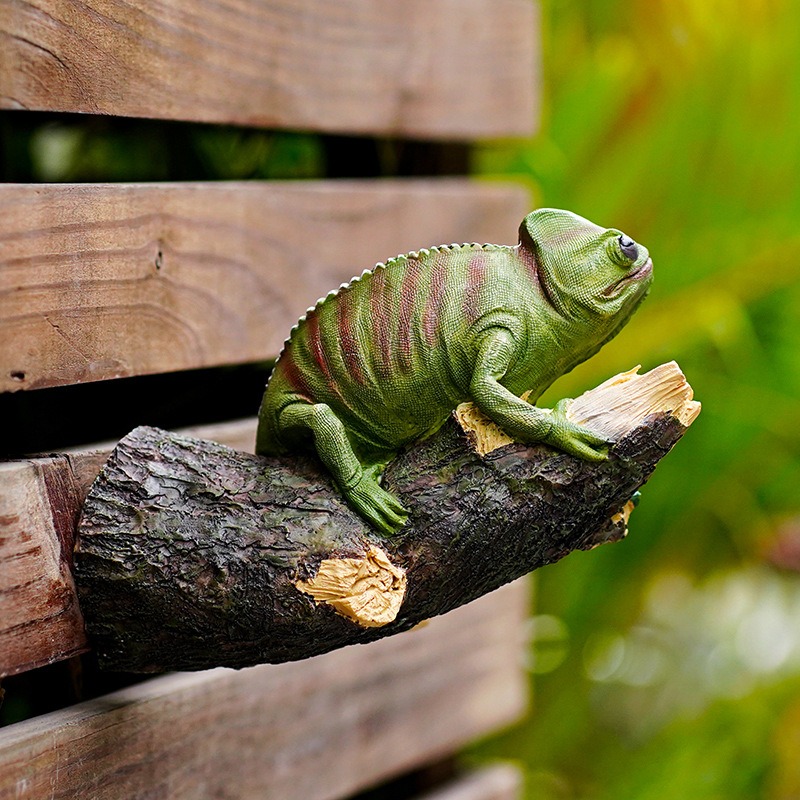 Chameleon ornament resting on a log across a weathered fence rail