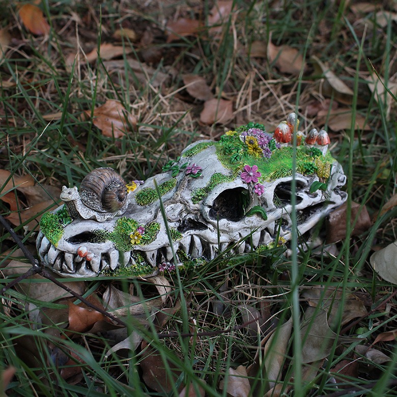 Dragon skull ornament resting on grass beside dry leaves in a garden