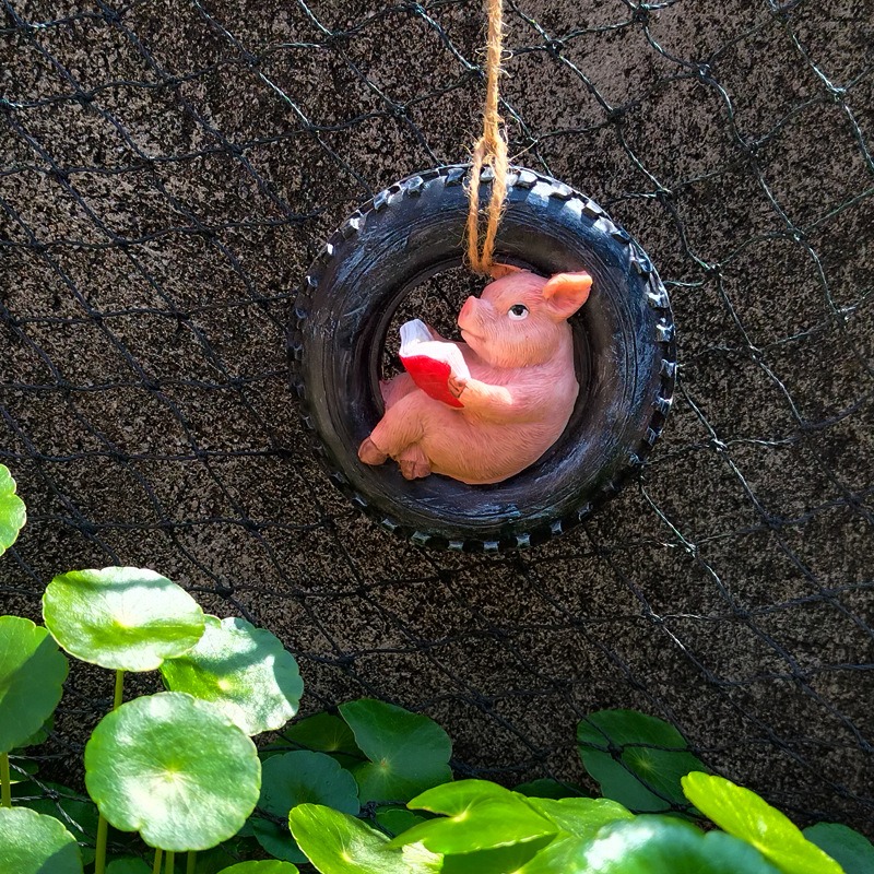 Pig ornament hung on a black wire mesh fence with green leaves in foreground