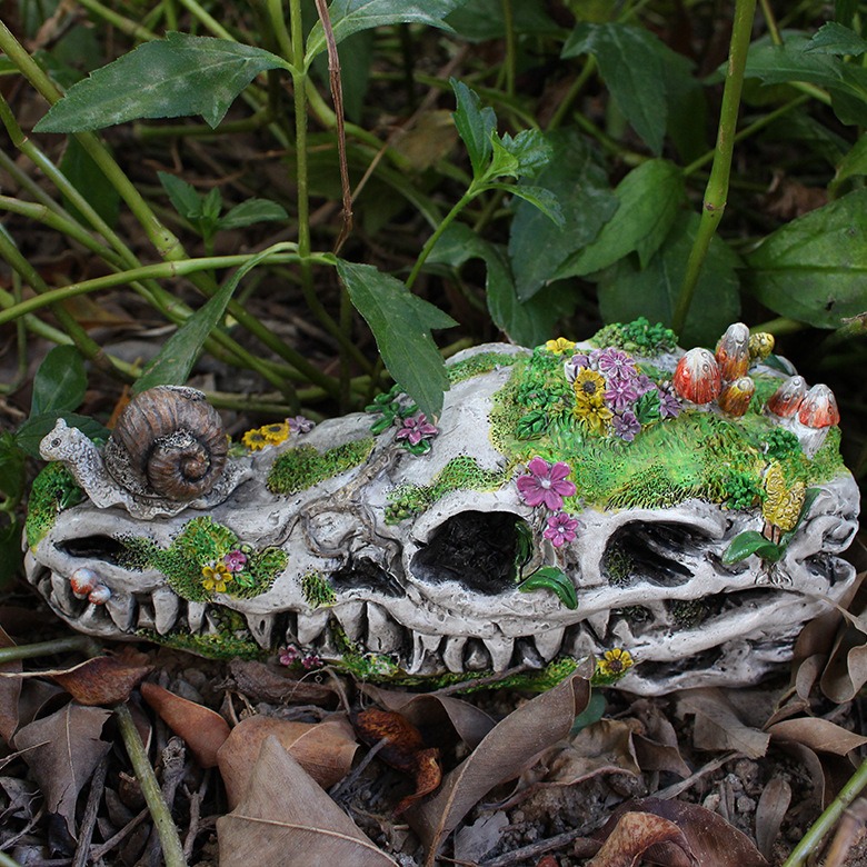 Close view of dragon skull with moss, flowers, butterfly and mushrooms among plants