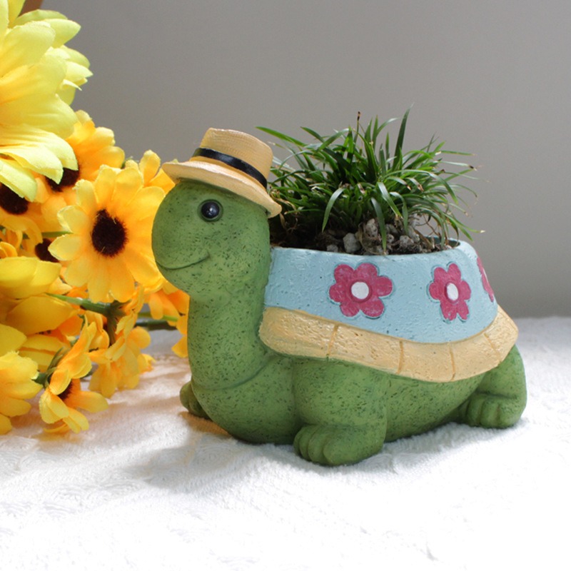 Turtle planter with grass tuft on white fabric beside yellow daisies