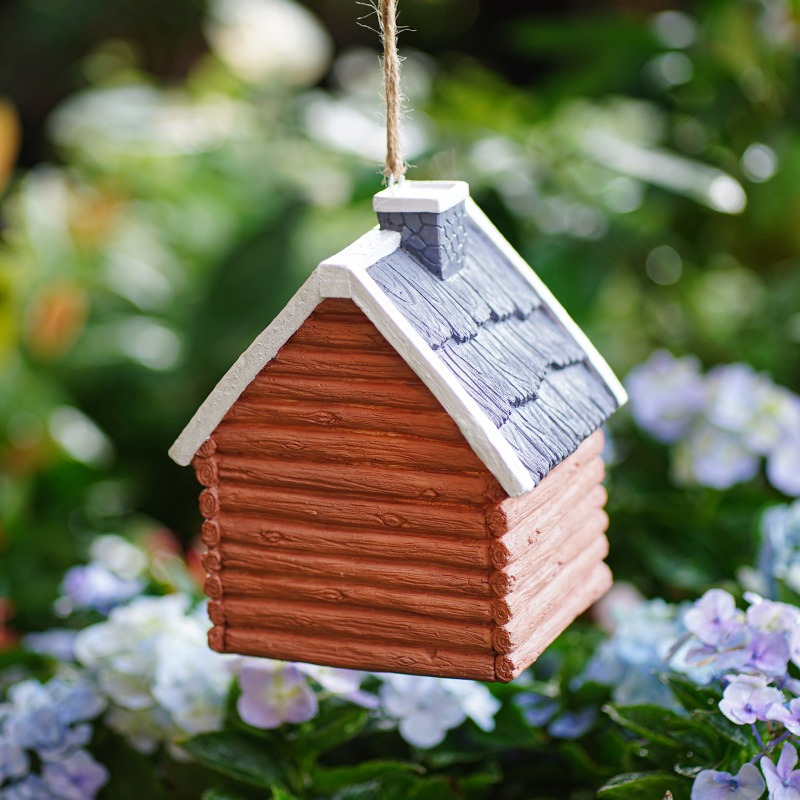 Bird house hanging by jute cord in front of green foliage and hydrangeas