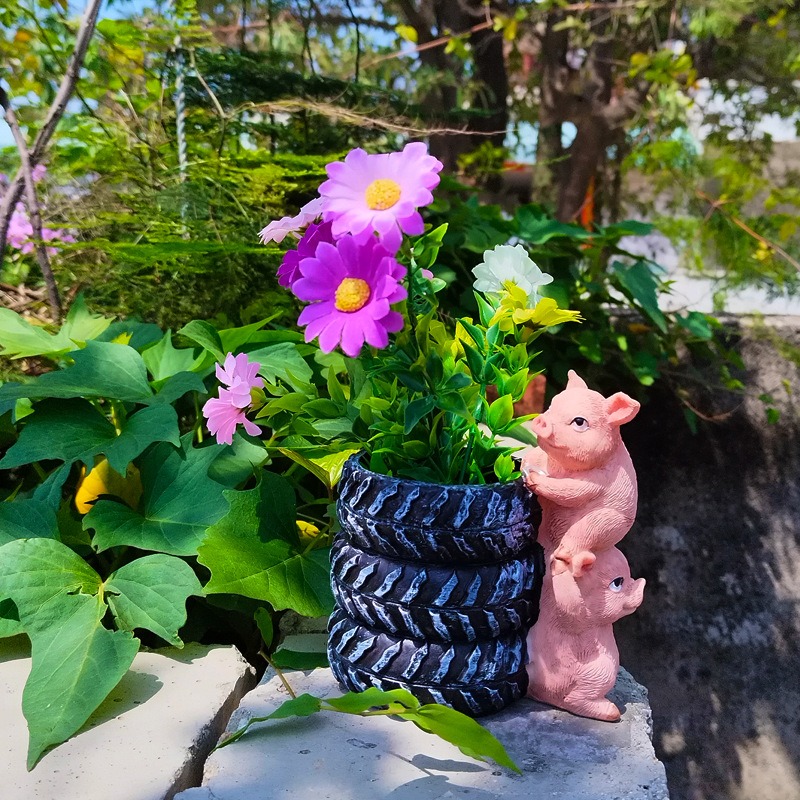 Tyre planter with pink pigs and purple and white daisies among green leaves