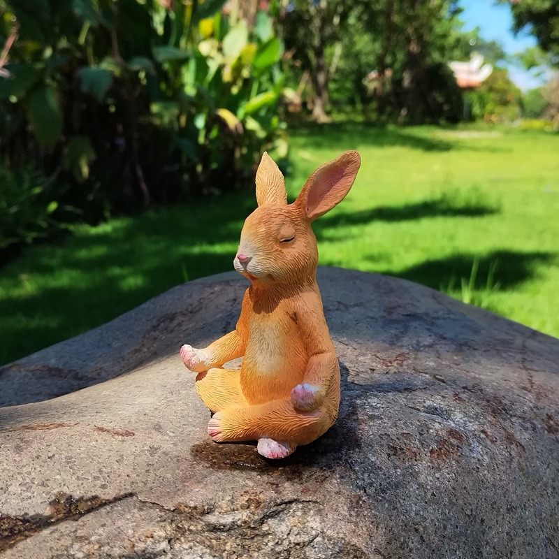 Seated bunny garden figurine resting on a rock beside lawn