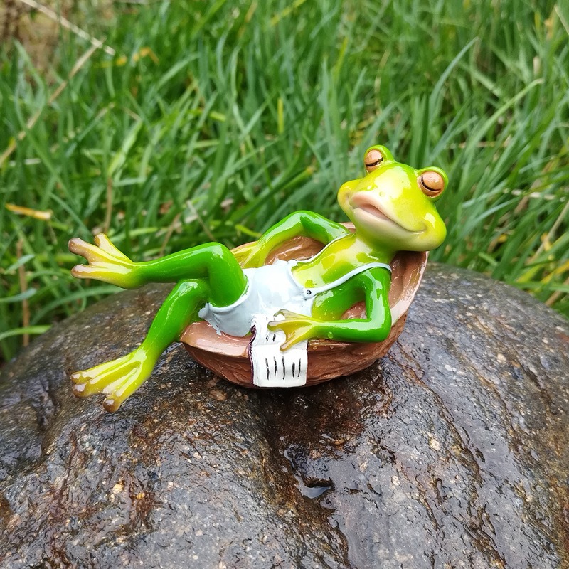 Glossy frog figurine reading on stacked books outdoors