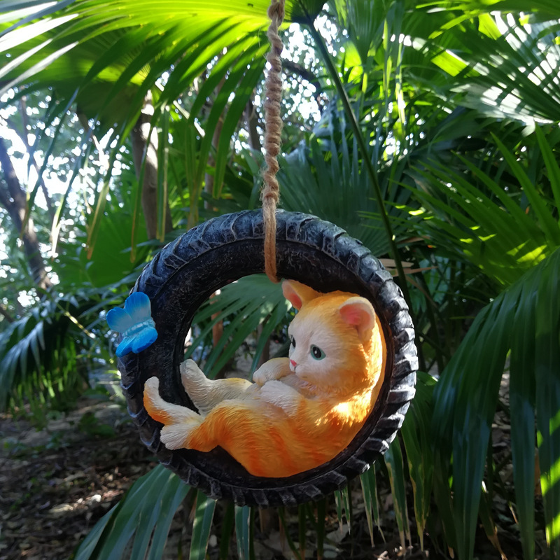 Ginger kitten lounging in a tire swing hung from jute rope outdoors