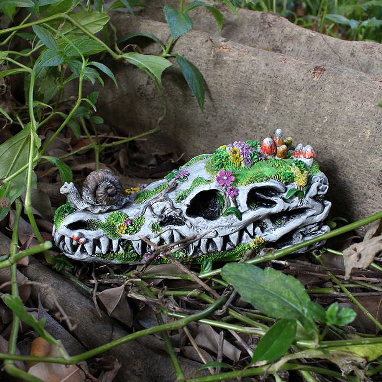 Skull statue nestled among green leaves and fallen timber in a garden bed